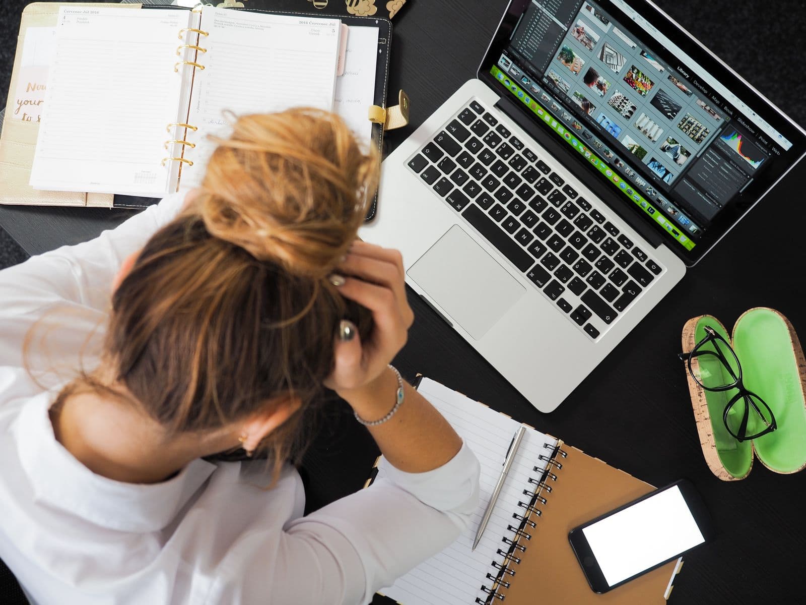 A small-business owner juggling a laptop, phone, and notebooks at once.